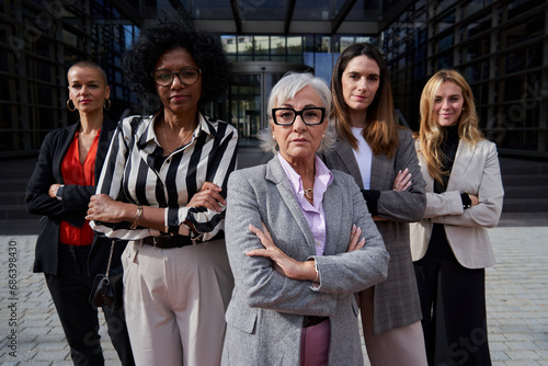 Empowered group of multiracial businesswomen headed by a mature caucasian woman, looking at camera with confidence, standing outdoors corporative district.