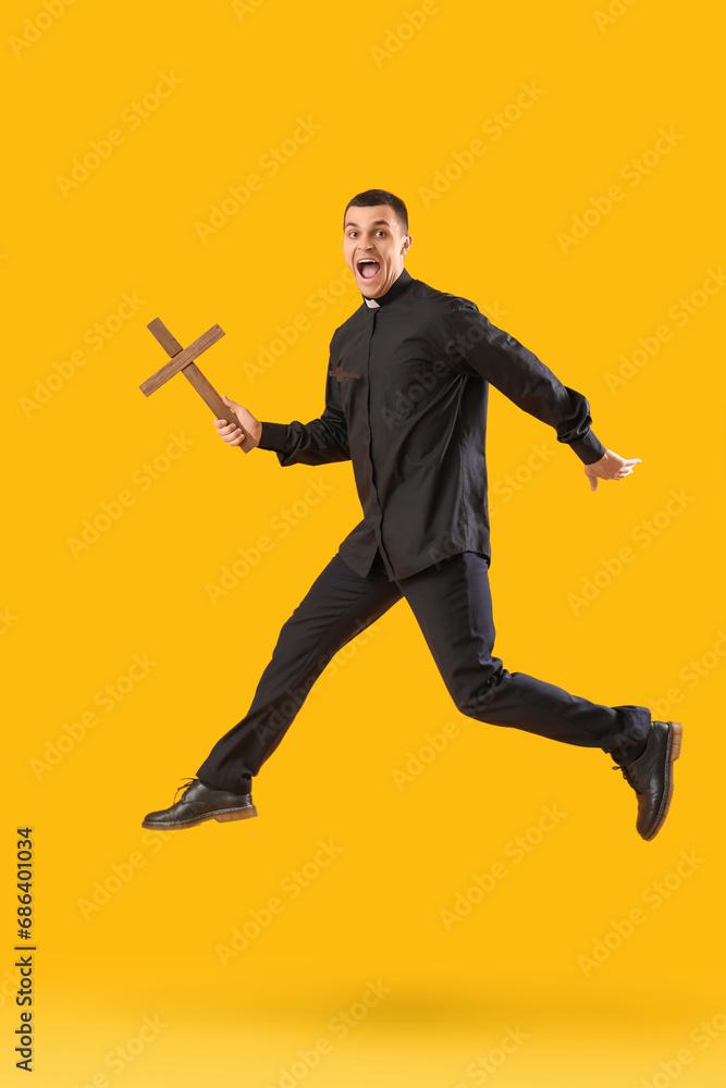 Young priest with cross jumping on yellow background Young priest with cross jumping on yellow background