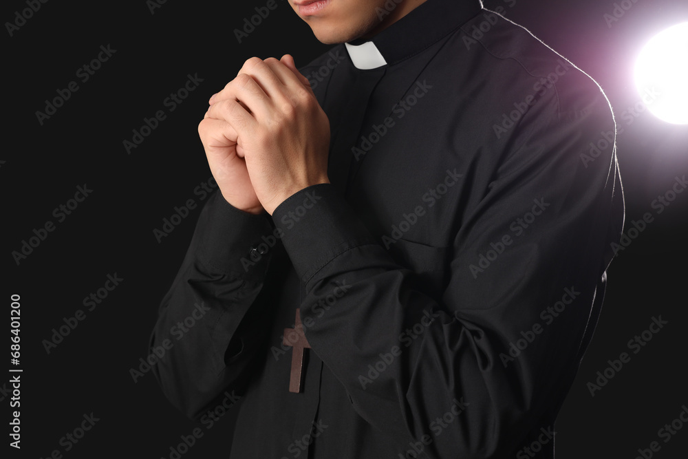 Young priest praying on dark background, closeup Young priest praying on dark background, closeup