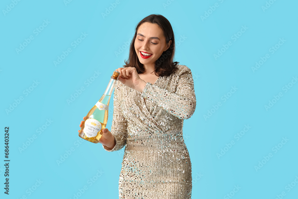 Beautiful young woman with champagne bottle on blue background Beautiful young woman with champagne bottle on blue background