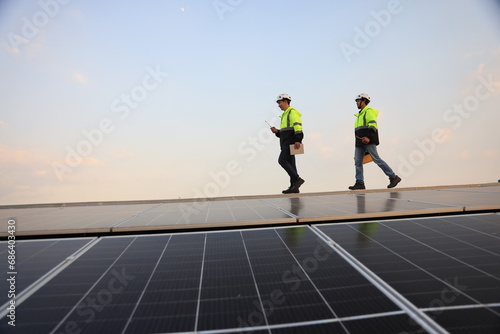 Two special Electrical engineers in safety suits worked and checked the solar system on the roof after installing, walking on the roof against the blue sky and photovoltaic panel.