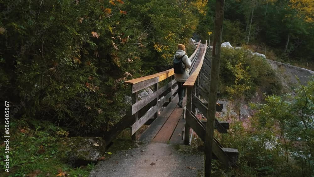 Beautiful female traveler walks across a bridge over a mountain river through the forest to the mountains. Incredibly beautiful views in the Alpine mountains. Hiking route in the Alps mountains in Beautiful female traveler walks across a bridge over a mountain river through the forest to the mountains. Incredibly beautiful views in the Alpine mountains. Hiking route in the Alps mountains in