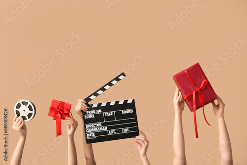 Female hands with Christmas gifts, movie clapper and reel on color background photo