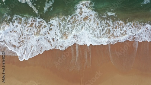 Fototapeta Naklejka Na Ścianę i Meble -  Sea wave on beach aerial view. Coast with waves as background from top view. Wave with sea foam background from drone. Aerial view of beach with waves of sea water
