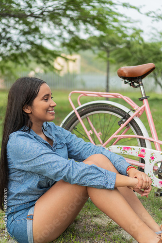 Woman sitting next to her classic bicycle on a sunny afternoon in the park.