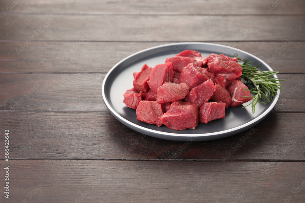 Pieces of raw beef meat with rosemary on wooden table. Space for text Pieces of raw beef meat with rosemary on wooden table. Space for text