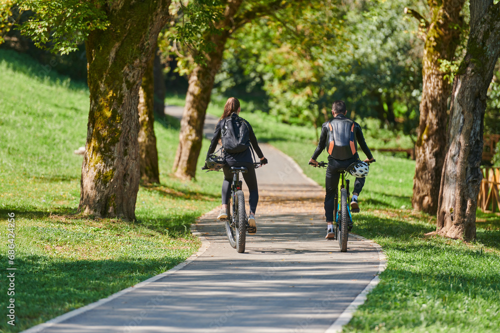 A blissful couple, adorned in professional cycling gear, enjoys a romantic bicycle ride through a park, surrounded by modern natural attractions, radiating love and happiness