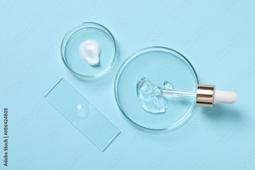 Fototapeta premium Petri dishes with samples of cosmetic serums and pipette on light blue background, flat lay