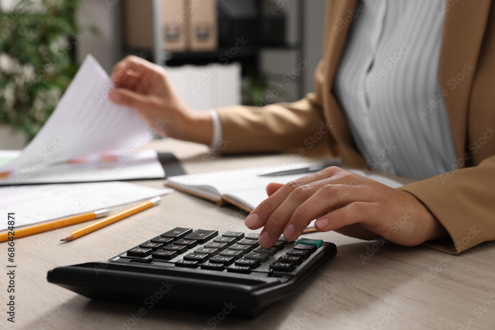 Woman using calculator while working with document at wooden table, closeup Woman using calculator while working with document at wooden table, closeup