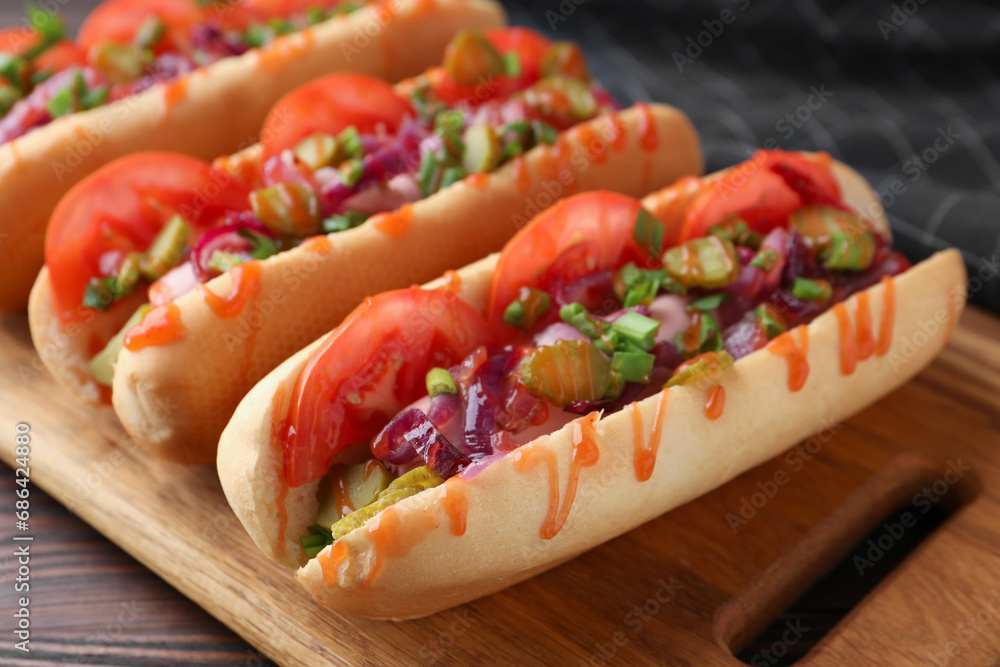 Tasty hot dogs with green onion, tomato, pickles and sauce on wooden table, closeup Tasty hot dogs with green onion, tomato, pickles and sauce on wooden table, closeup