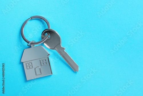 Key with keychain in shape of house on light blue background, top view. Space for text © New Africa