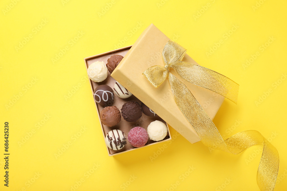 Open box with delicious chocolate candies on yellow background, top view Open box with delicious chocolate candies on yellow background, top view