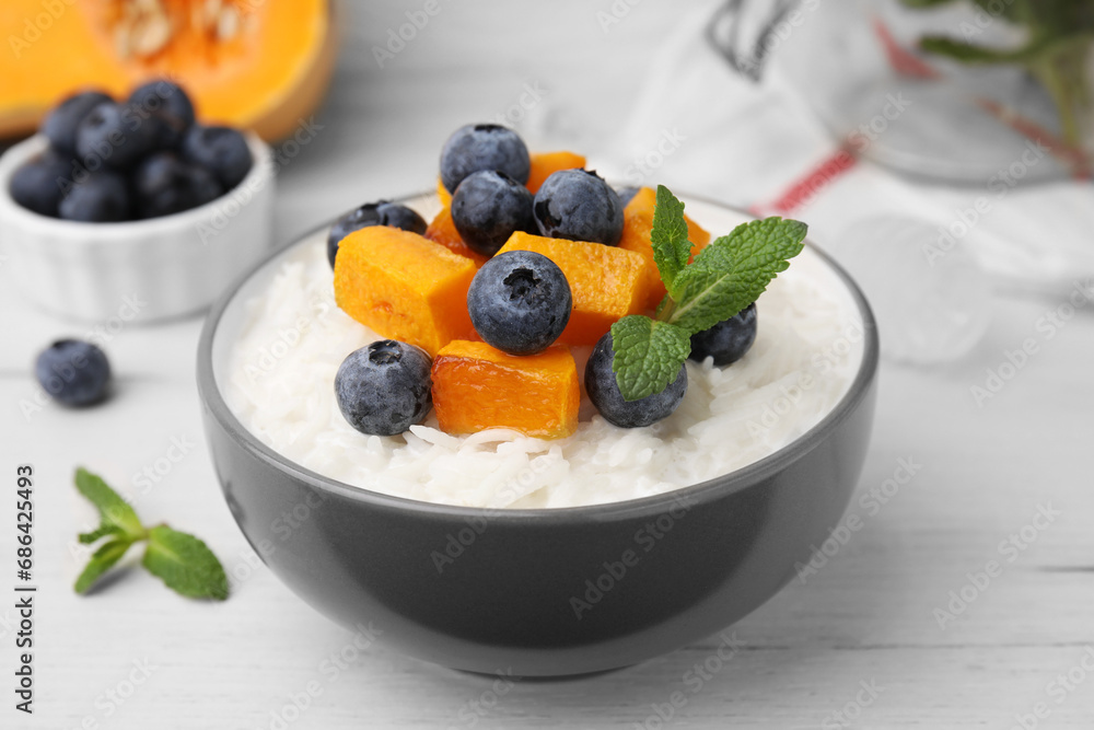 Bowl of delicious rice porridge with blueberries, pumpkin and mint on white table, closeup