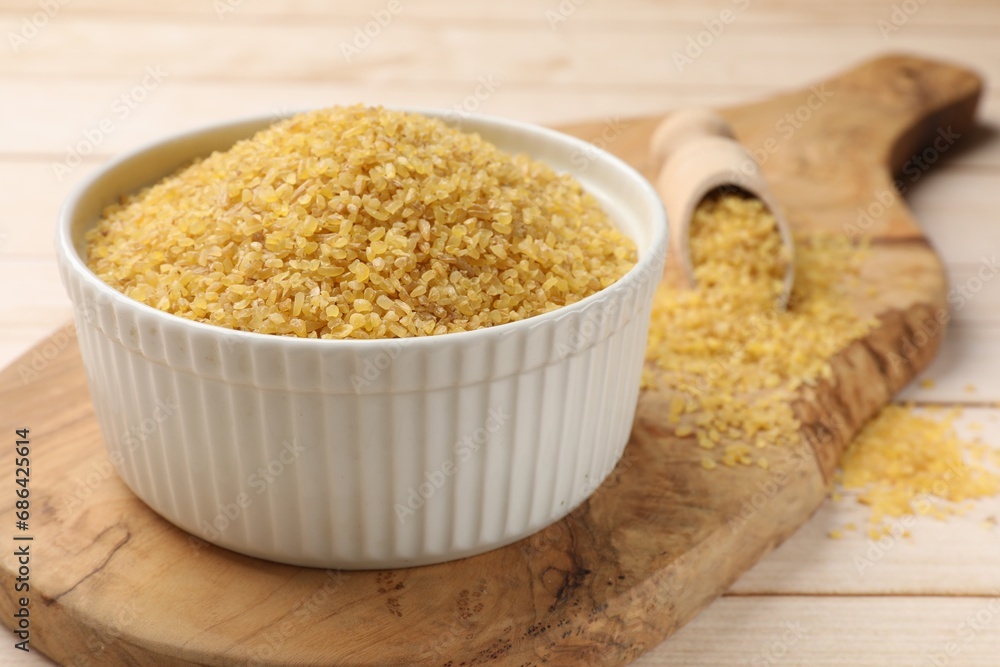 Bowl and scoop with raw bulgur on light wooden table, closeup Bowl and scoop with raw bulgur on light wooden table, closeup