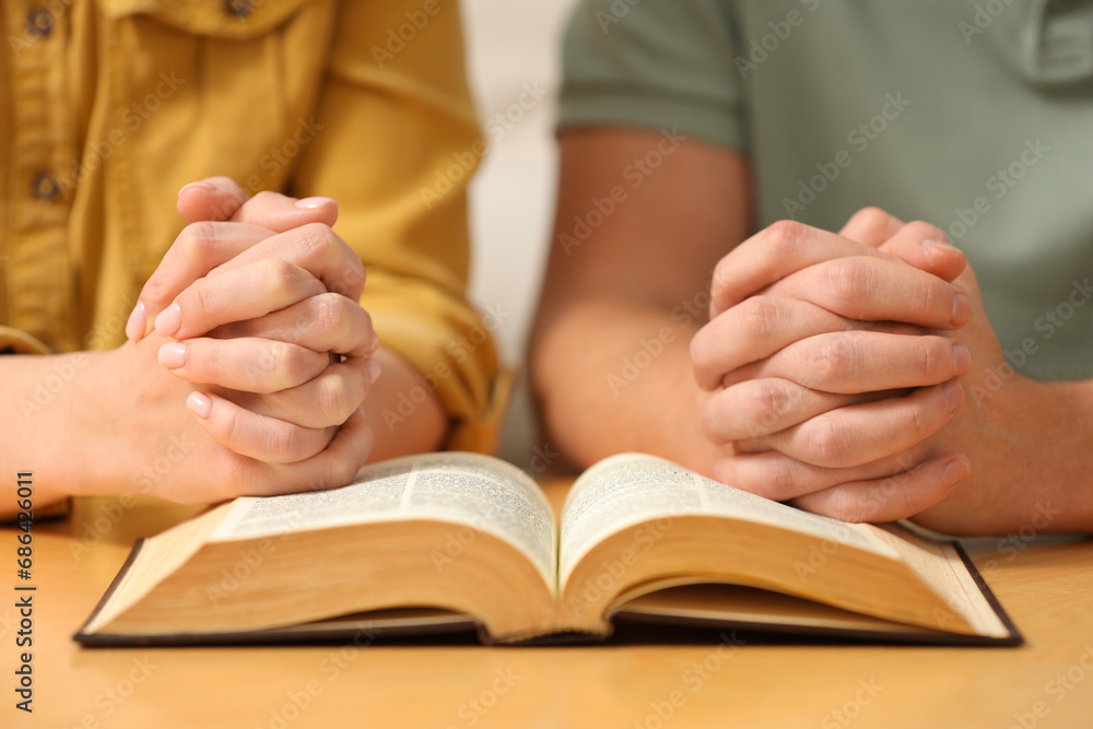 Family couple praying over Bible together at table indoors, closeup Family couple praying over Bible together at table indoors, closeup