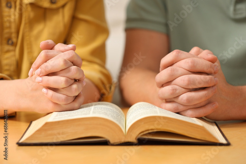 Family couple praying over Bible together at table indoors, closeup