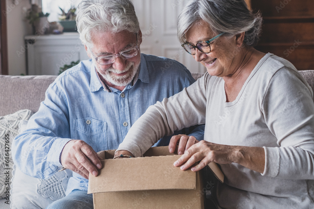 Happy mature aged older family couple unpacking carton box, satisfied