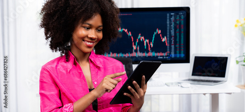 Analytical young African American businesswoman, a specialist in successful stock exchange trading, against dynamic data graph displaying marketing trend analysis on screen. Tastemaker. photo