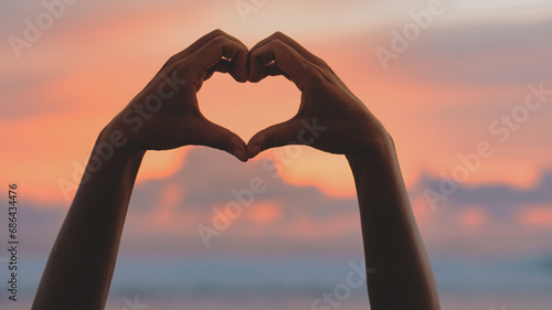 Hands forming a heart shape with sunset silhouette