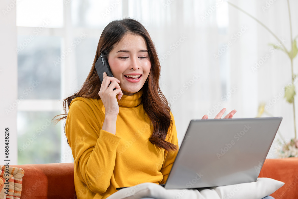Asian woman multitasks seamlessly working with laptop while engaging in professional phone conversation with a customer at home,display of efficiency and excellent customer service. Small Business. Asian woman multitasks seamlessly working with laptop while engaging in professional phone conversation with a customer at home,display of efficiency and excellent customer service. Small Business.