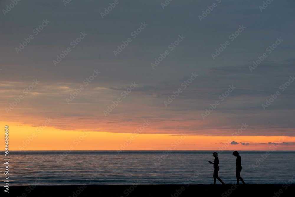 Two people walking on the shore at sunset