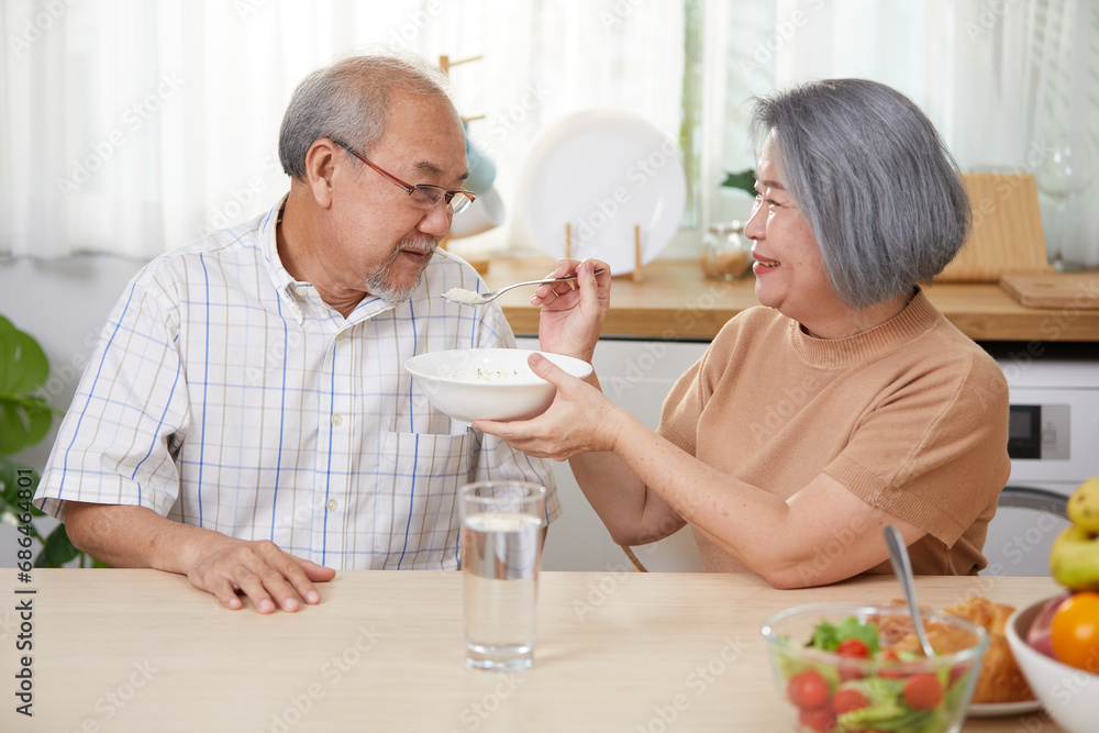 senior woman feeding rice porridge to senior man in the kitchen senior woman feeding rice porridge to senior man in the kitchen