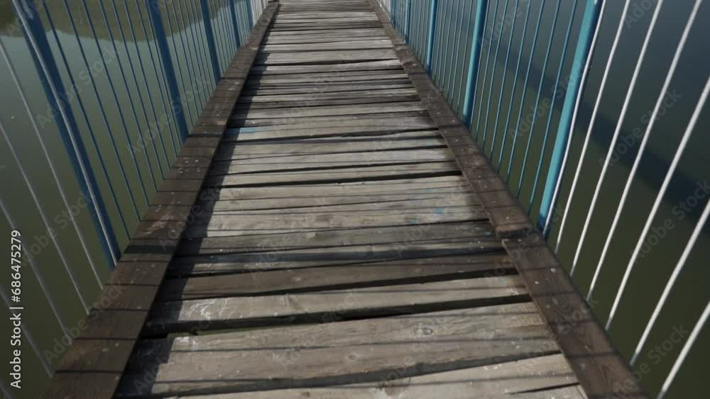 Camera moves forward revealing a narrow bridge with steel blue railings and suspenders over a murky body of water. Camera moves forward revealing a narrow bridge with steel blue railings and suspenders over a murky body of water.
