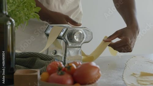 Medium close up shot of Homemade pasta being made. Woman making pasta using pasta machine. Fresh traditional italian fettuccini comimg out of pasta maker. Tagliatelle maker home made.