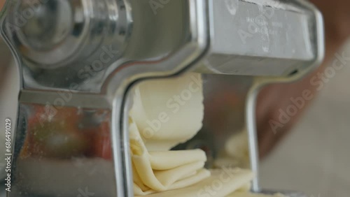 pasta machine making dough layers. pasta maker makes thin pieces of dough using a mechanical manual kitchen machine. cooking traditional way pasta. chefs hand rotates pasta machine handle. close-up