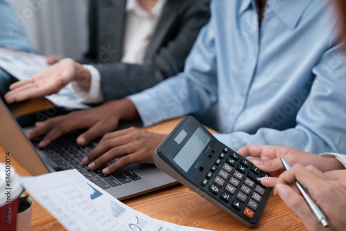 Multiracial analyst team use calculator and data science BI Fintech dashboard data to analyze financial report on office meeting table. Diverse business people for analytic teamwork. Concord