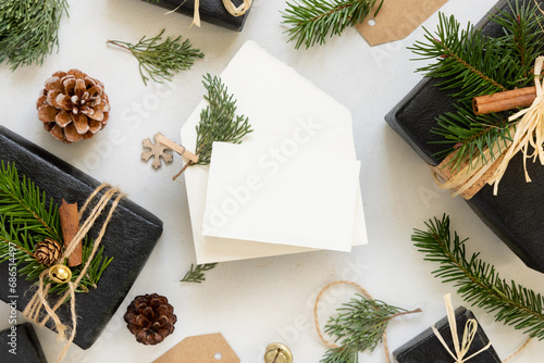 Envelope and card near Christmas decor, gift boxes and green fir branches, mockup