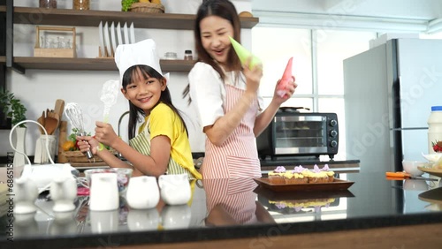 Small girl enjoying making cake with her mother in kitchen at home