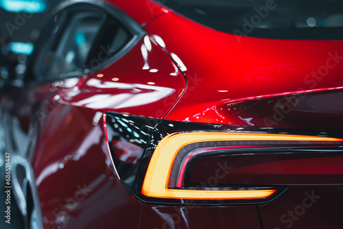 Close-up of a modern red crossover automobile with LED red taillights. The rear window of a red car that is parked on the street is detailed from the outside. © chartphoto