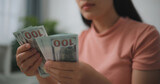Portrait of Happy young asian woman counts cash dollar bills while sitting in living room at home,counting stack cash money dollar