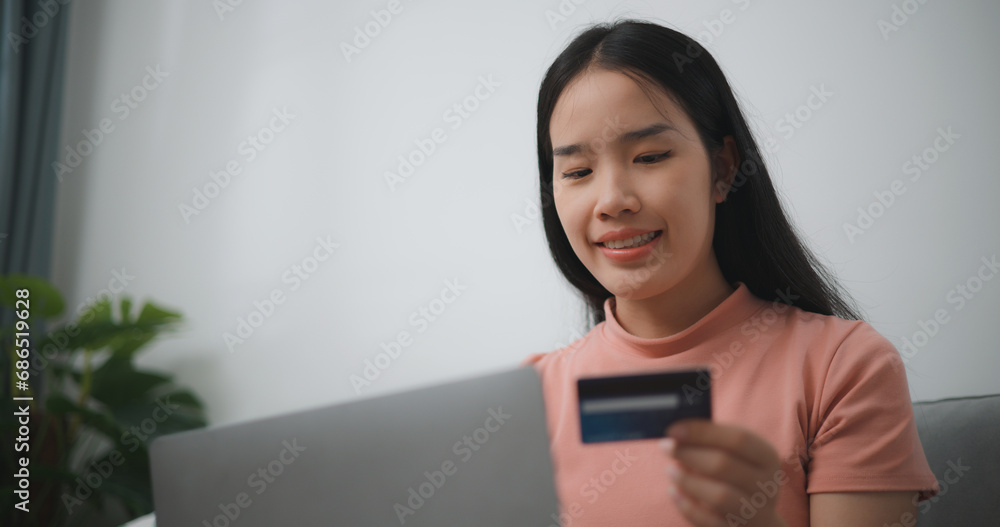 Portrait of Young asian woman sitting on sofa in living room, makes online banking payments through the internet from bank card on laptop,Shopping online with credit card. Portrait of Young asian woman sitting on sofa in living room, makes online banking payments through the internet from bank card on laptop,Shopping online with credit card.