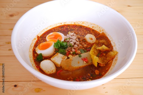 Delicious Tom Yum noodles with eggs ready to eat on white bowl on wooden table background.