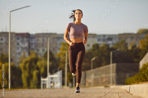 Portrait of a young sporty woman running alone in an urban area in city park. Fit athlete girl runner exercising outdoors training for marathon jogging in nature. Fitness, workout outdoor concept.