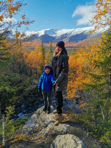 A girl with a child on the background of the autumn Arctic landscape in the Khibiny mountains. Kirovsk, Kola Peninsula, Polar Russia. Autumn colorful forest in the Arctic