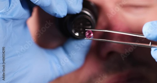 Jeweler holding pink diamond in hands and looking at it with magnifying glass closeup 4k movie slow motion. Determination of quality of gemstones concept photo