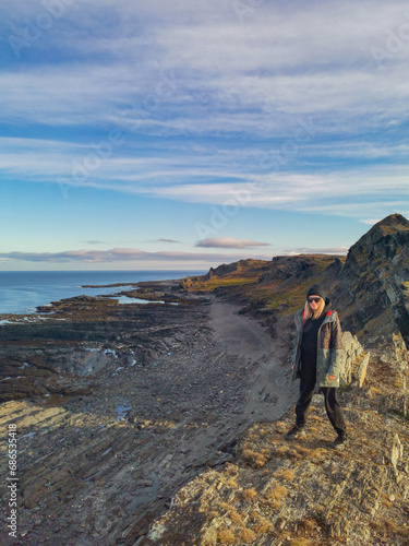 A woman on the background of the rocky coast of the Barents Sea. Beautiful view of the cliffs and the coast of the Rybachy and Sredny peninsulas. The harsh beauty of the north.