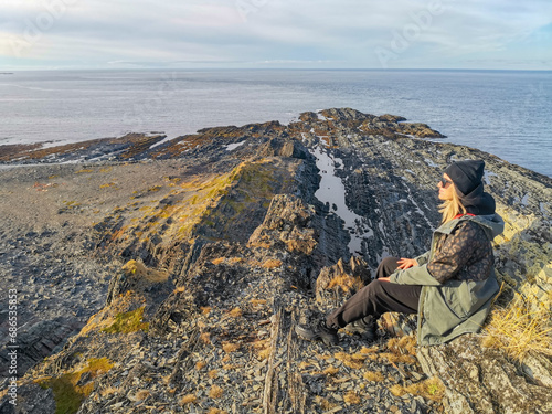 A woman on the background of the rocky coast of the Barents Sea. Beautiful view of the cliffs and the coast of the Rybachy and Sredny peninsulas. The harsh beauty of the north. © Виктория Балобанова