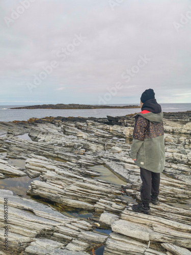 A woman on the background of the rocky coast of the Barents Sea. Beautiful view of the cliffs and the coast of the Rybachy and Sredny peninsulas. The harsh beauty of the north. photo