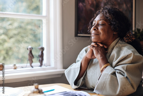 Mature woman with eyes closed and hands on chin sitting at home photo