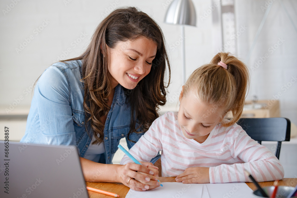 Mother and daughter learning together at home, sitting at the desk in front of a computer. Back to school Mother and daughter learning together at home, sitting at the desk in front of a computer. Back to school