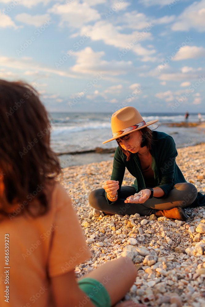 child collects shells and pebbles on a sandy beach with a caring, kind and beautiful mother in a hat on vacation. Family having fun on the beach collecting shells.