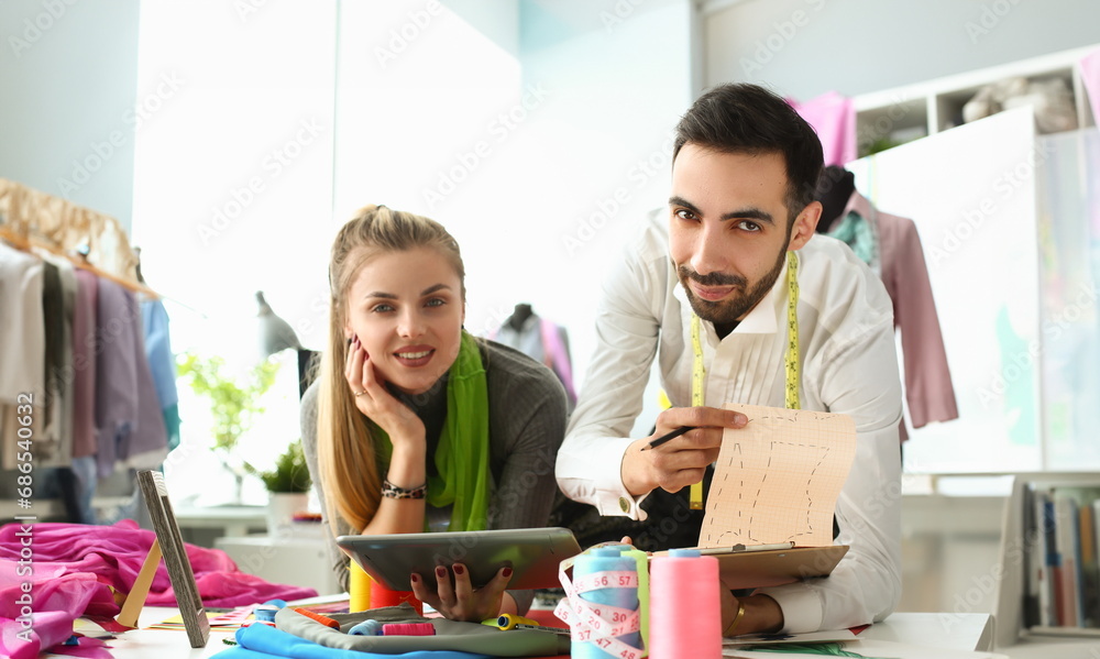 Φωτογραφία Young business woman stylist seamstress holding tablet male colleague showing sketches of clothes