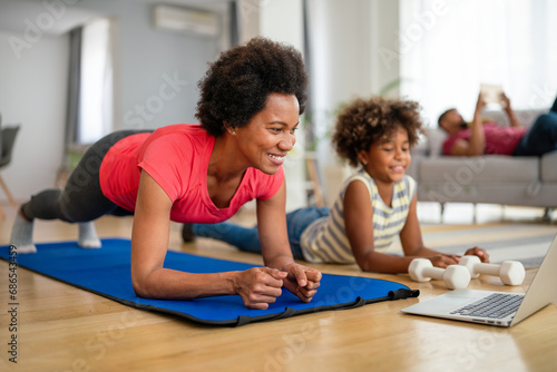 Happy young mother and daughter practicing yoga together at home, enjoying healthy lifestyle