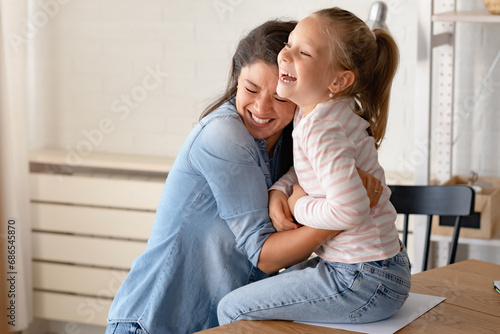 A child loves her mother. Cheerful smiling mother and daughter cuddling, hugging, and having fun at home. Mothers day photo