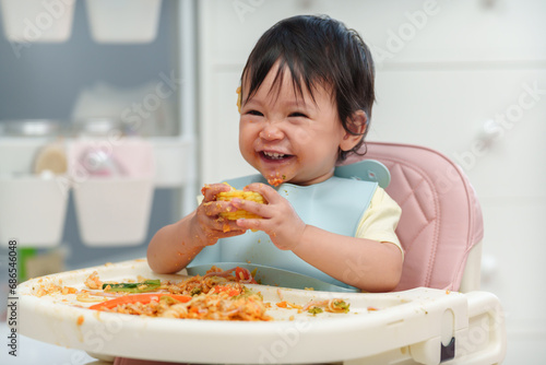 happy infant baby eating food and vegetable by self feeding BLW or baby led weaning on chair photo