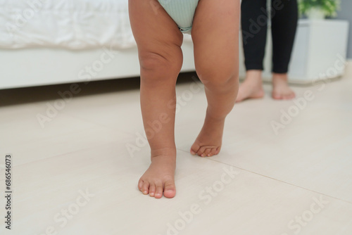close up leg of infant baby walking with mother helping